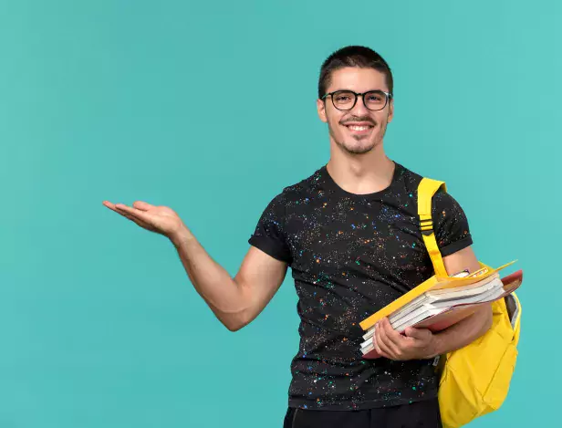front-view-of-male-student-in-dark-t-shirt-yellow-backpack-holding-files-and-books-smiling-on-light-blue-wall