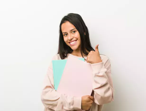young-hispanic-woman-holding-some-notebooks-smiling-raising-thumb-up